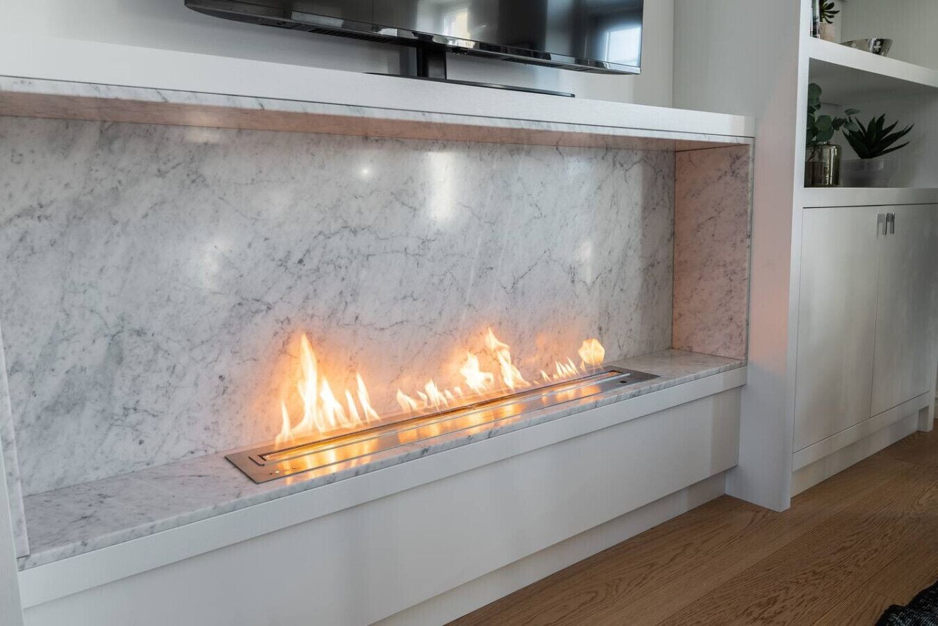 Una cocina moderna con chimenea integrada, armarios blancos y un televisor de pantalla plana montado encima.