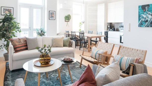 A modern living room with a sofa, coffee table, and chairs, a dining area with a table and chairs, and a kitchen in the background. - Luxury Penthouse | Sauna | Balcony | AirCon (Helsinki)