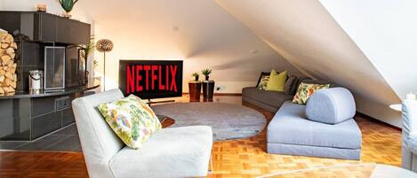 Un loft moderne doté d’une cheminée, d’un grand téléviseur diffusant du contenu « NETFLIX » et d’un coin salon confortable agrémenté d’un tapis à motifs.