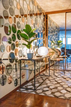 Ein modernes Interieur mit Wandmuster, einer Glastrennwand und einer Sitzecke mit Pflanze und Dekorationselementen.