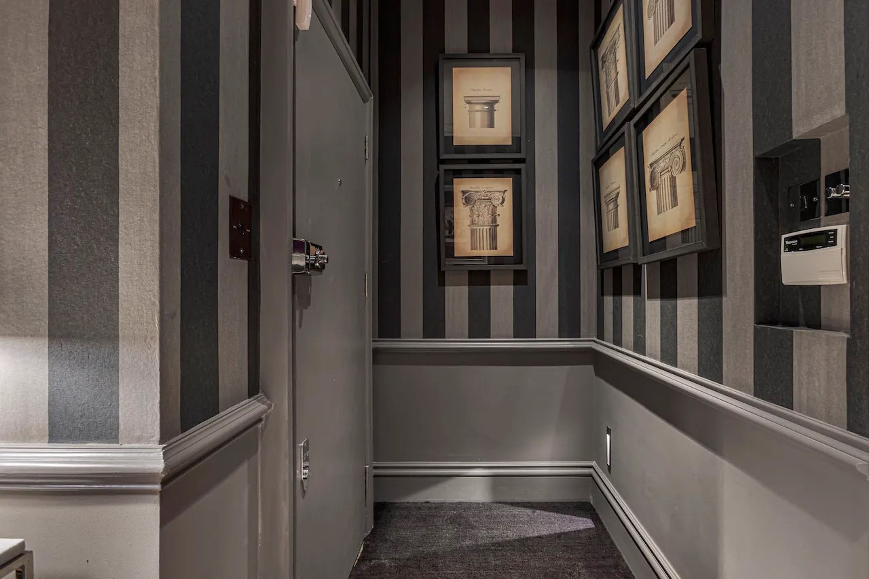 A hallway with striped walls, framed architectural drawings, and a thermostat on the wall.