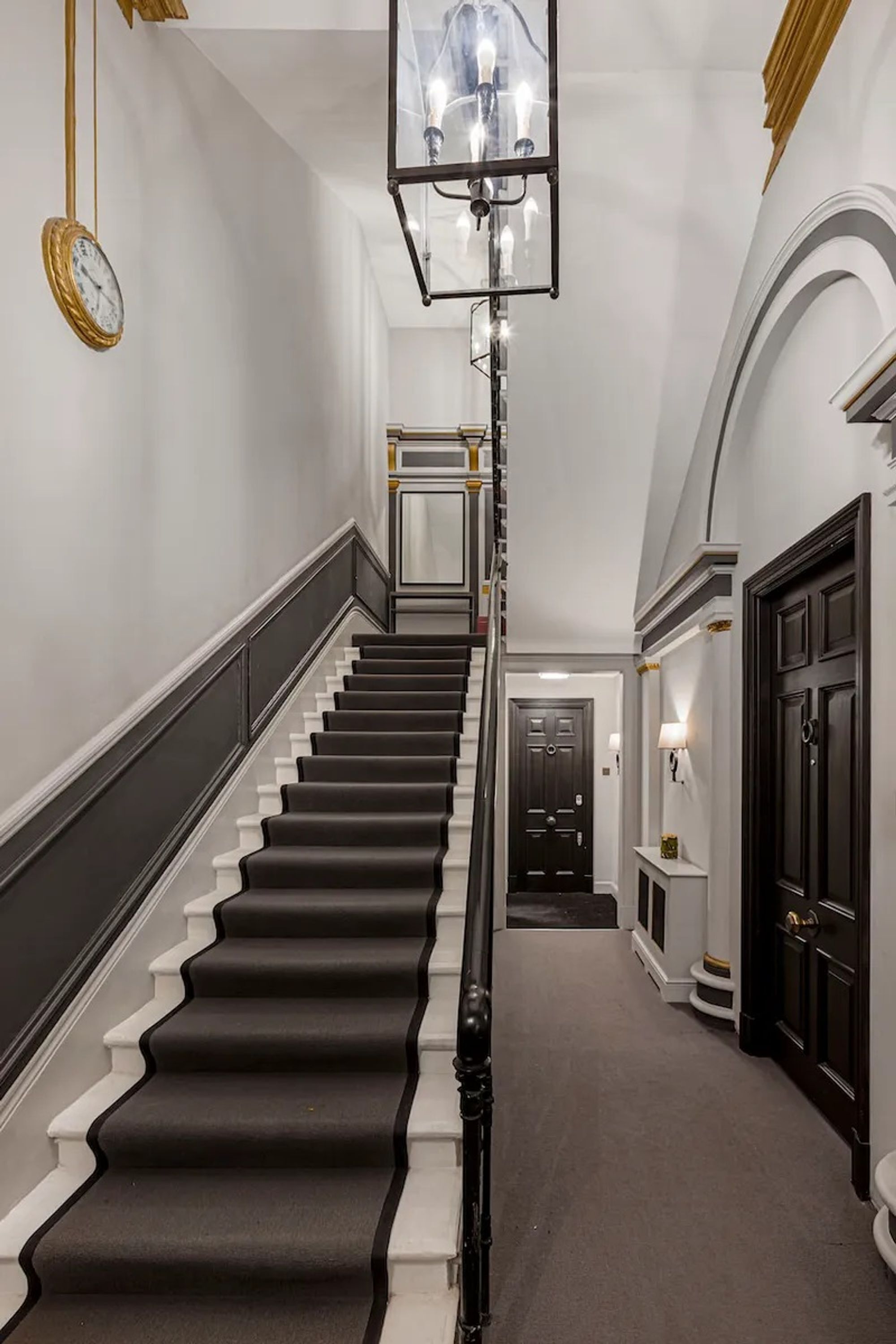 A grand staircase with black and white steps, a chandelier, and a clock on the wall.