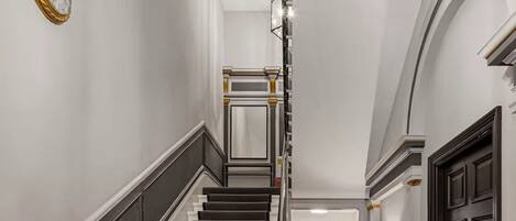 A grand staircase with black and white steps, a chandelier, and a clock on the wall.