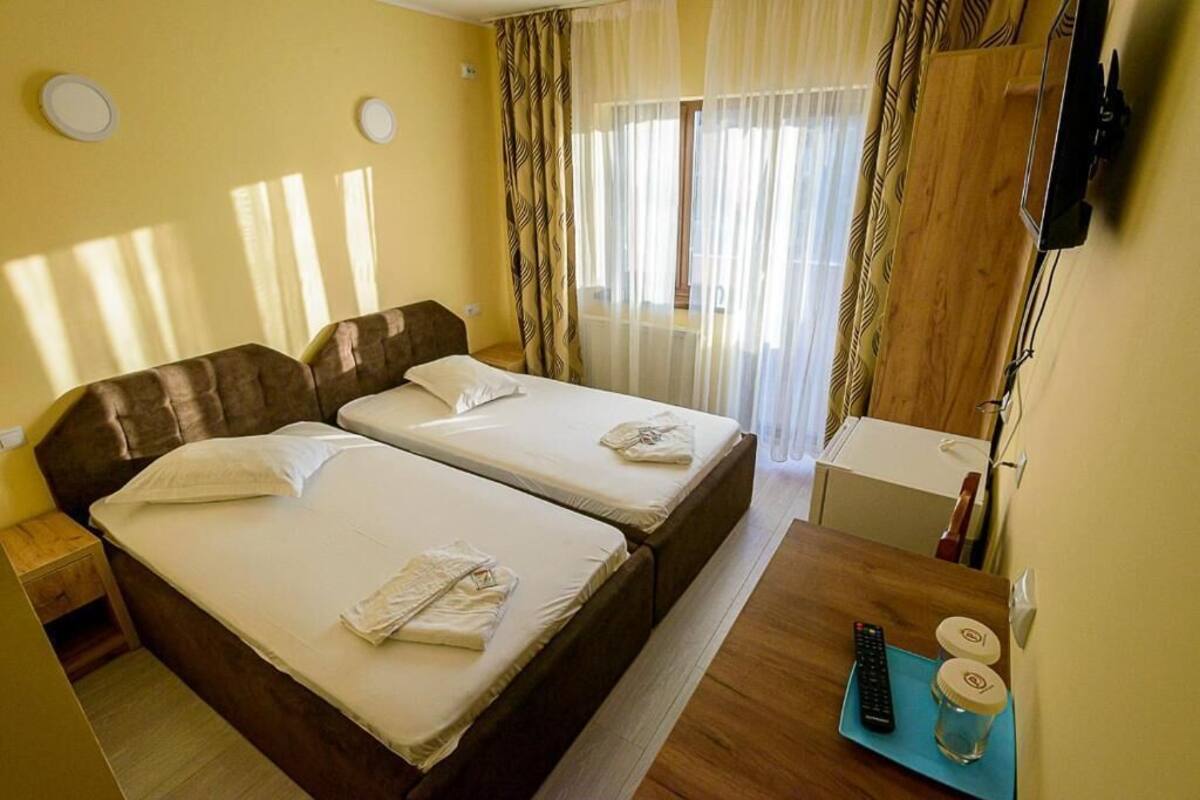 A hotel room with two beds, a small desk, a TV, and a window with curtains.