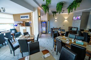 Un restaurante con una zona de recepción, asientos y una pantalla de televisión.