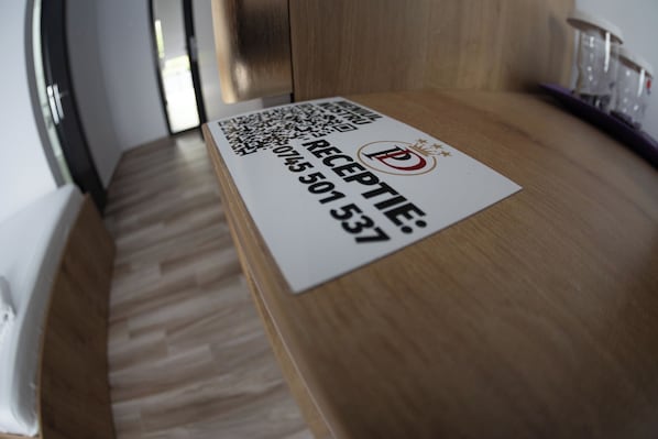 A reception desk with a sign displaying a QR code and a phone number. - Casa Domneasca Riana (Pitești)