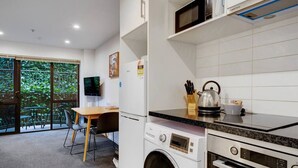 A compact kitchen with a washing machine, microwave, and oven. There's a dining area with a table and chairs, and a TV mounted on the wall.