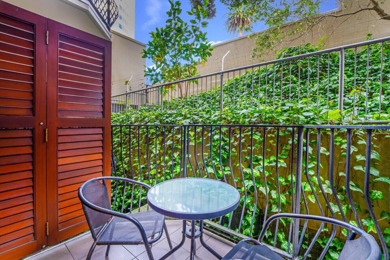 A balcony with a wooden door, metal railing, and a glass table with two chairs.
