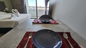 Une chambre d’hôtel avec un lit parfaitement fait, une table à manger dressée avec une assiette bleue, un set de table rouge, une fourchette et une cuillère.