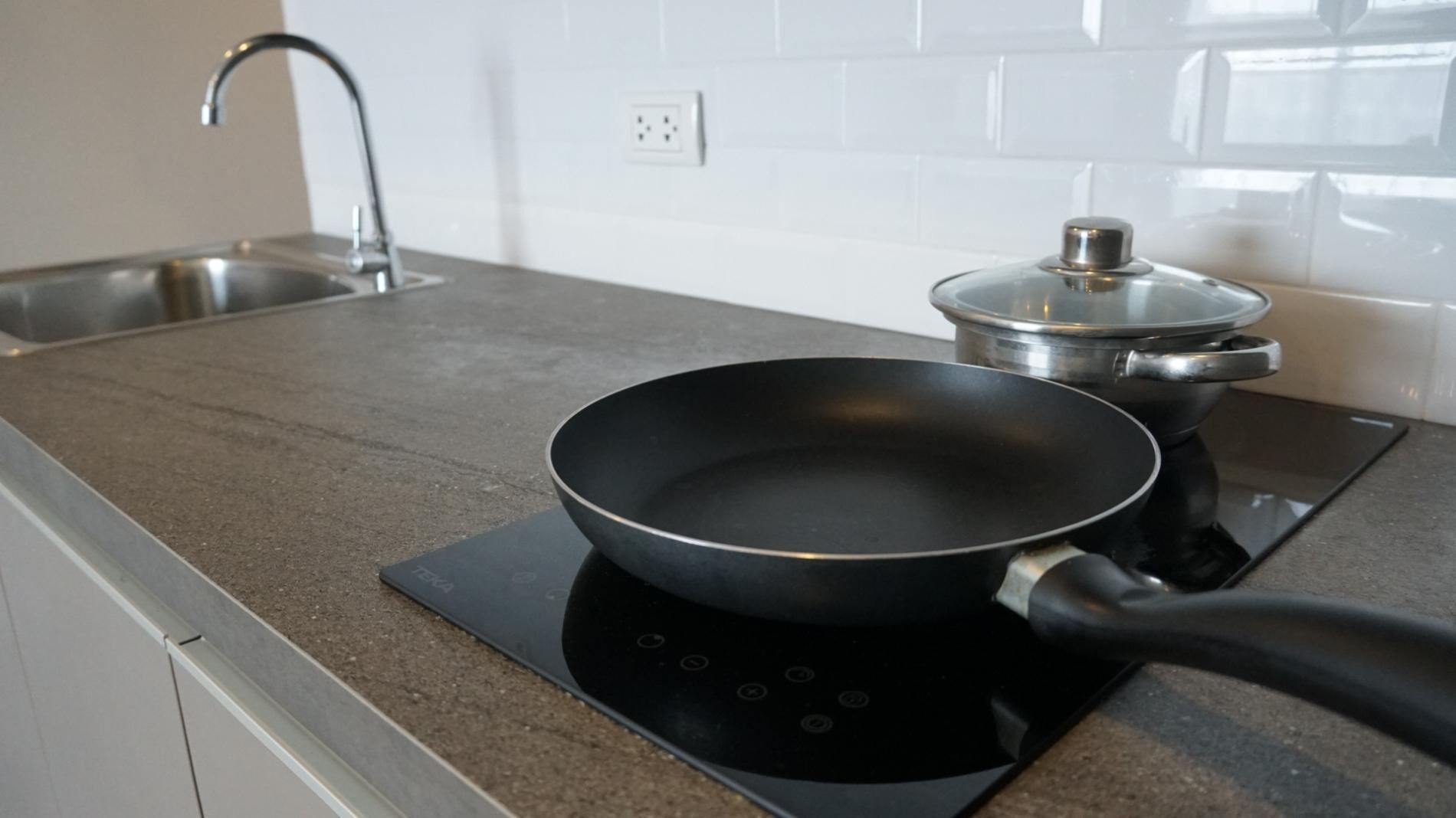 Une cuisine avec une plaque de cuisson à induction noire, une poêle et une casserole sur la plaque.