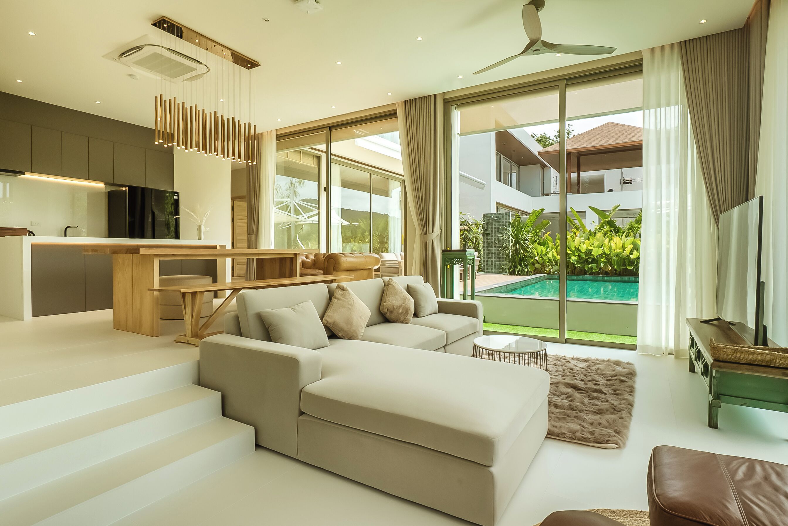 A modern living room with a large sectional sofa, a dining area, and a view of a swimming pool.