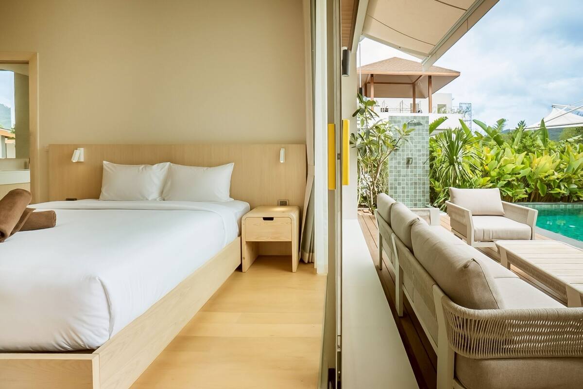 Una habitación de hotel moderna con una cama grande, una mesita de noche, una pequeña mesa y vistas a una piscina y zonas verdes.