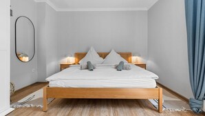 Una cama bien hecha con cabecera de madera, dos lámparas de noche y un espejo grande en la pared.