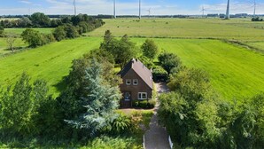 Una casa rural rodeada de campos verdes exuberantes y aerogeneradores al fondo.