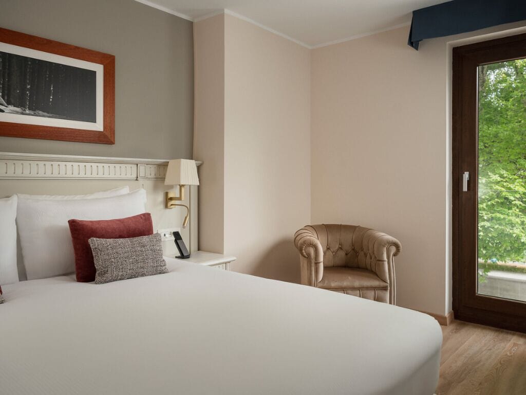 Habitación de hotel con una cama grande, una silla, una mesita de noche, una lámpara y un cuadro en la pared.