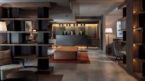 Un espace dâaccueil moderne comprenant un comptoir de rĂ©ception, trois employĂ©s et un coin salon avec des tables et des chaises.