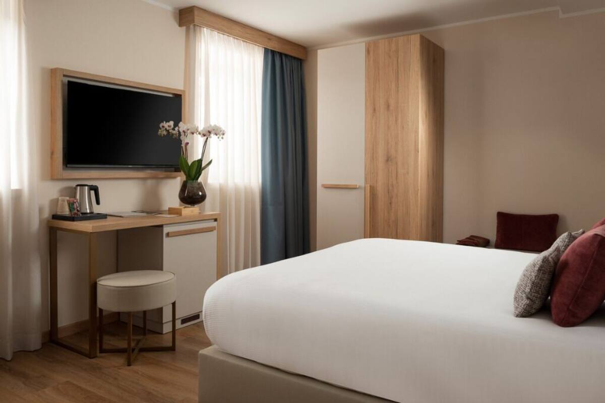 Une chambre d’hôtel comprenant un lit, un bureau avec une chaise, une télévision et une fenêtre avec des rideaux.