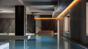 A modern indoor pool area with a clear water surface, a marble wall, and a wooden bench. - Hotel Livata Mountain Wellness  (Subiaco)