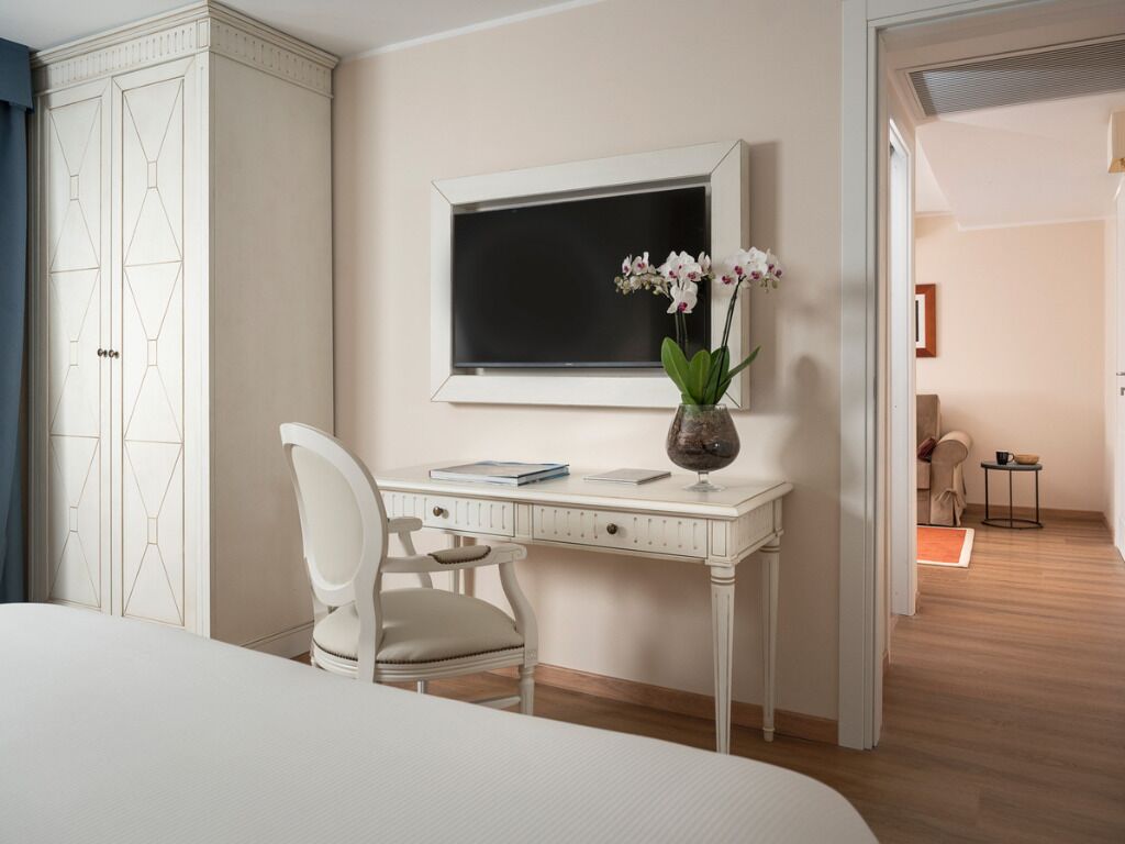 Un dormitorio con una cama, un escritorio blanco con una silla, un florero con flores y un cuadro en la pared.