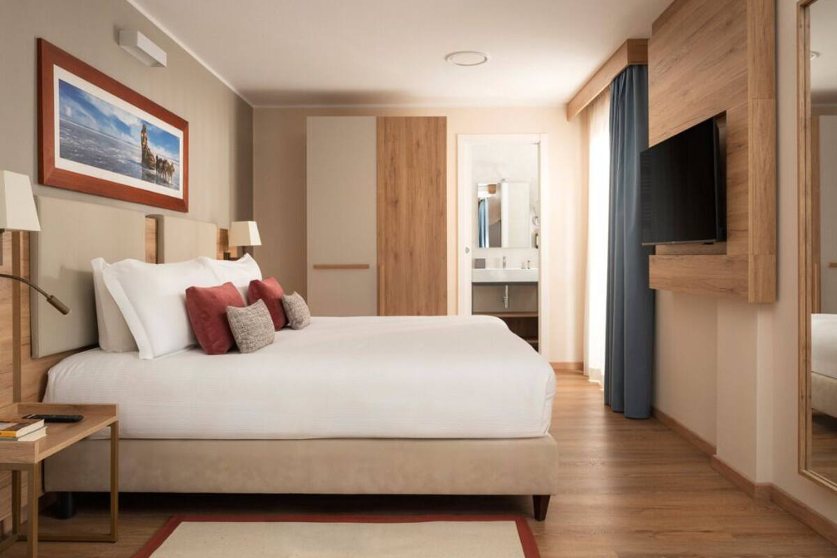 Une chambre d’hôtel avec un lit, des lampes de chevet, un téléviseur, un mur recouvert de panneaux de bois et un tableau encadré.