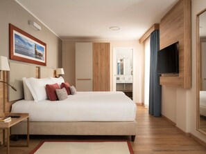 Une chambre d’hôtel avec un lit, des lampes de chevet, un téléviseur, un mur recouvert de panneaux de bois et un tableau encadré.