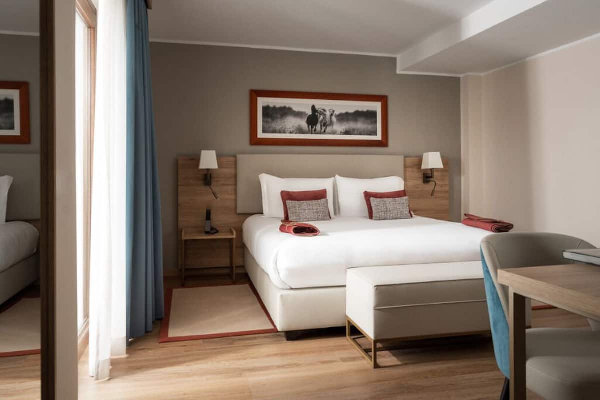 Une chambre d’hôtel avec un lit, des tables de chevet, un bureau et une chaise.