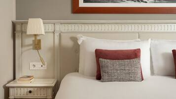 A neatly made bed with white linens and two pillows, one red and one grey, a bedside lamp, and a framed picture above the bed.
