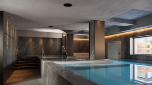 A modern indoor swimming pool with a stone wall, a seating area, and a staircase. - Hotel Livata Mountain Wellness  (Subiaco)