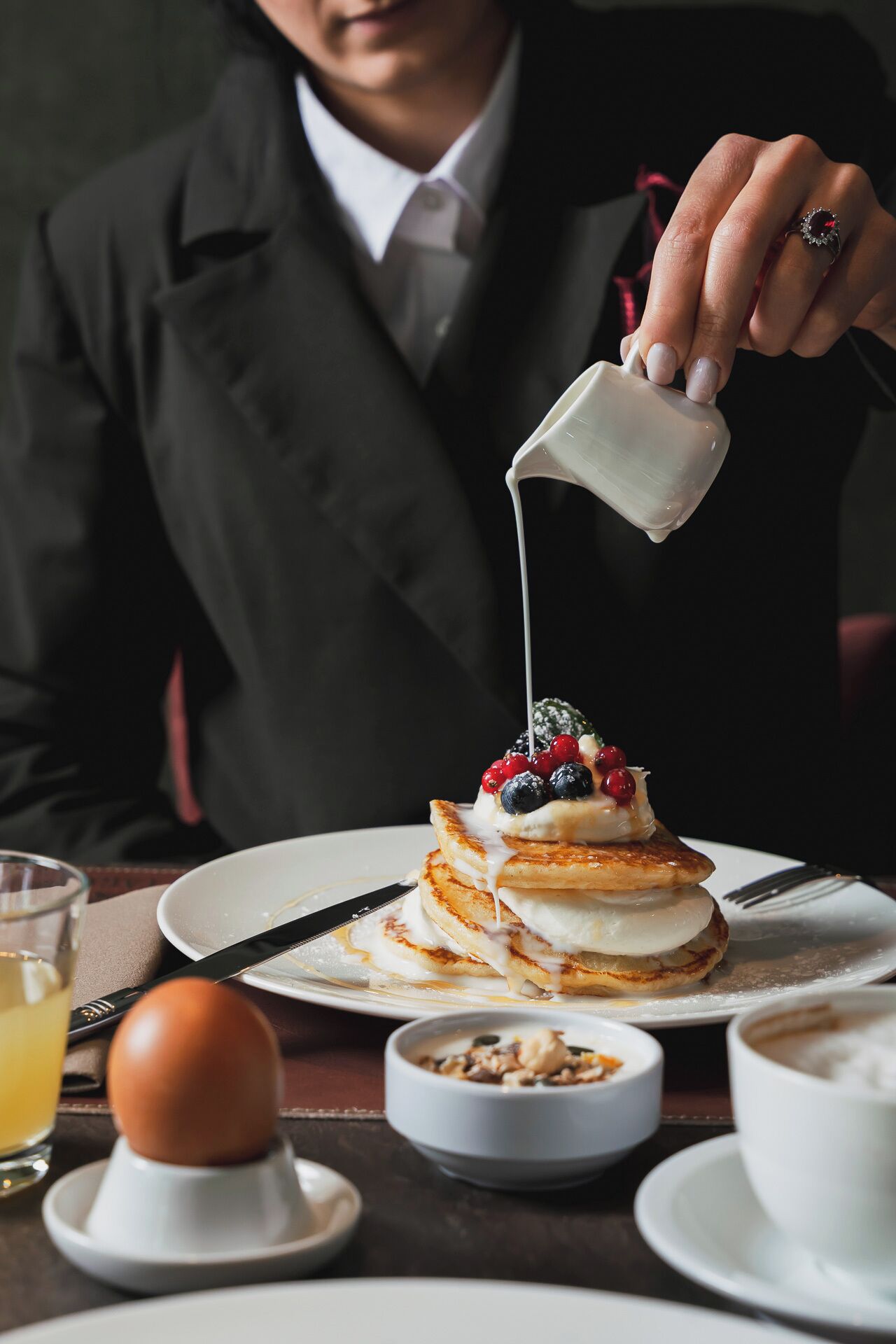 A breakfast setting with pancakes, berries, and a pouring milk pitcher.