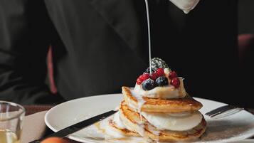 A breakfast setting with pancakes, berries, and a pouring milk pitcher.