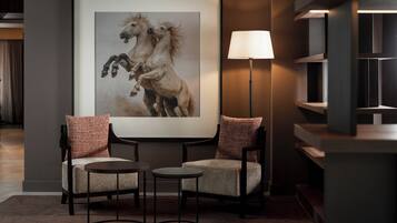 Una moderna hall d'albergo con un'opera d'arte incorniciata raffigurante cavalli, due poltrone, una lampada da terra e una mensola a design minimalista.