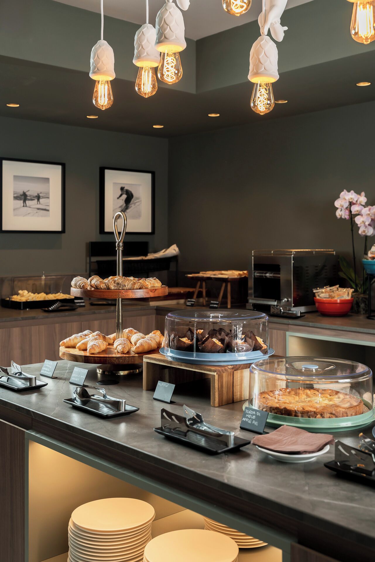 A buffet with various pastries and desserts, a coffee machine, and a seating area with framed pictures.