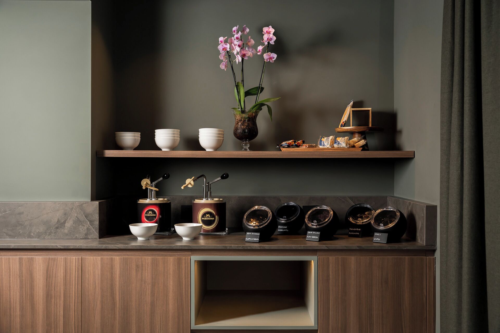 A kitchen counter with a coffee grinder, a vase with flowers, and a shelf with bowls and a wooden tray.