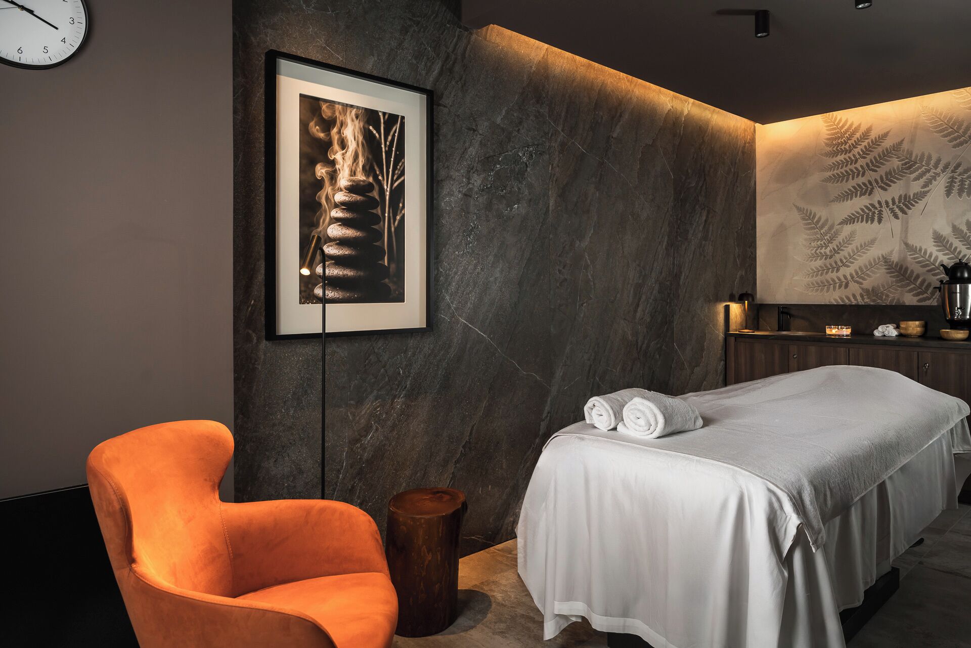 Une chambre à coucher moderne avec un lit, une chaise, un tableau encadré et un mur orné d’un motif de fougère.