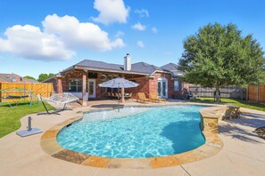 A backyard with a swimming pool, a brick house, and a hammock. - 5BR Pool House Near Dallas with Hot Tub & Game Room (Red Oak)