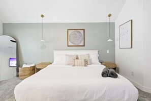 A neatly made bed with white bedding and two pillows, a small bedside table with a lamp, a wall-mounted artwork, and a framed picture. - 5BR Pool House Near Dallas with Hot Tub & Game Room (Red Oak)