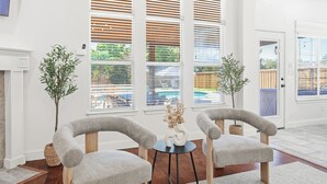 Een moderne woonkamer met twee grijze fauteuils, een kleine ronde tafel met een vaas en een open haard.