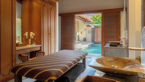 A spa room with a massage table, a large stone basin, and a view of an outdoor swimming pool. - Villa Elegant by Exotiq (Seminyak)