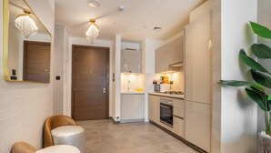 A modern kitchen with built-in appliances, a wooden door, and a potted plant. - Manzil - Stylish 1BR with Pool and Gym  (Dubai)