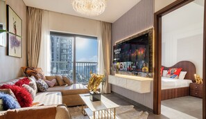 A modern hotel room with a large window, a sofa, a dining table, and a TV mounted on the wall. - Manzil - Stylish 1BR with Pool and Gym  (Dubai)