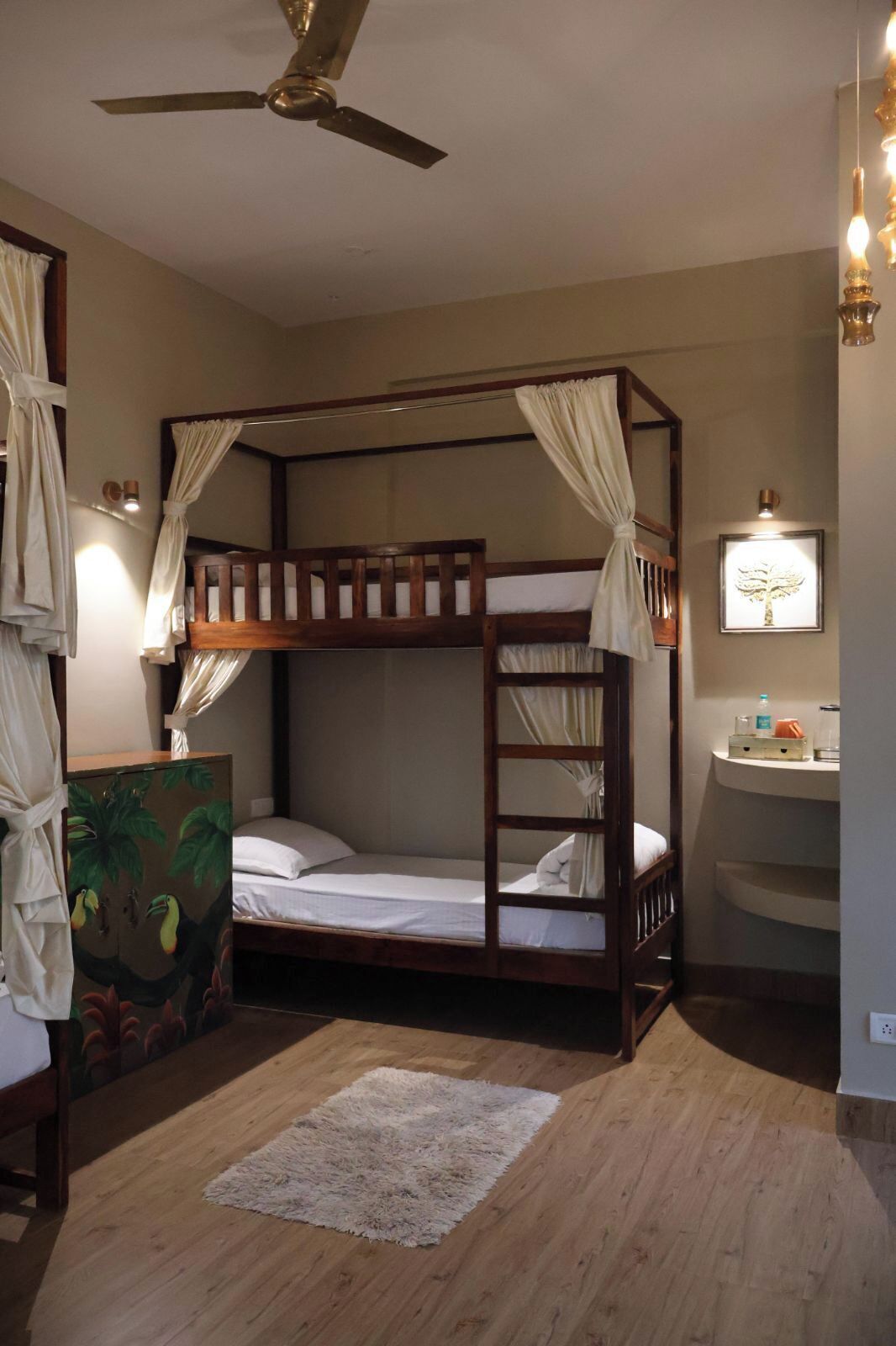 A bunk bed room with a ceiling fan, a small desk with a mirror, and a painting on the wall.