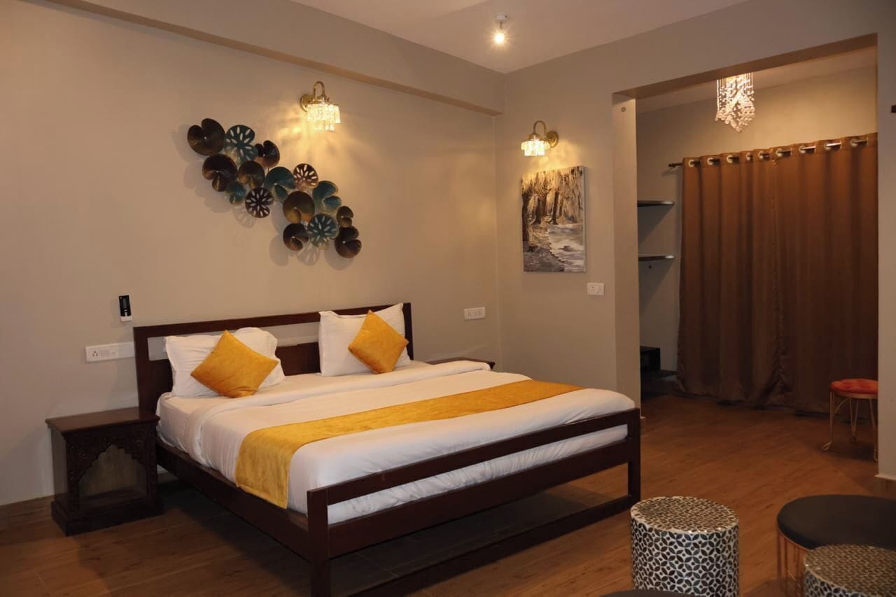 A neatly arranged bedroom with a large bed, two wall sconces, a decorative wall piece, and a view of a bathroom with a shower curtain.