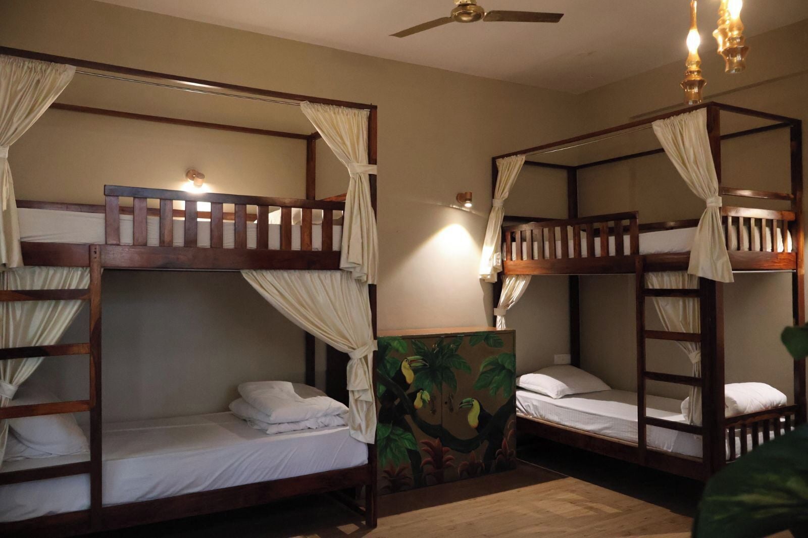 A room with two bunk beds, each with a canopy and a ladder. There is a ceiling fan and a wall-mounted light fixture.