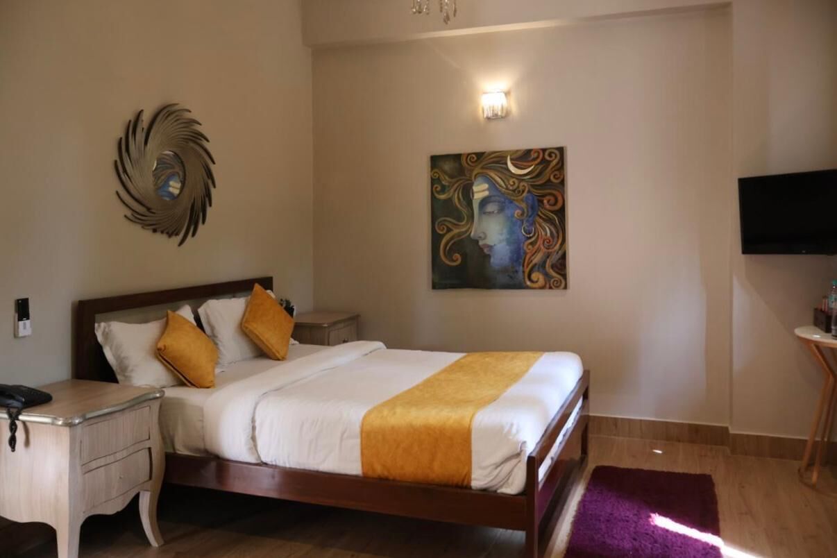 A hotel room with a wooden bed, a nightstand, a desk, a television, and a painting on the wall.