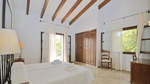 Ein Hotelzimmer mit einem großen Bett, Holzbalkendecke, einem Sessel und einem Fenster mit Vorhängen.