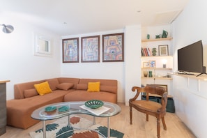 Una sala de estar moderna con un sofá marrón, una mesa de centro de vidrio, una silla de madera y un televisor de pantalla plana montado en la pared.