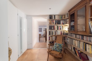 Una habitación con una estantería, un sillón con cojín y una puerta que da a otra estancia.
