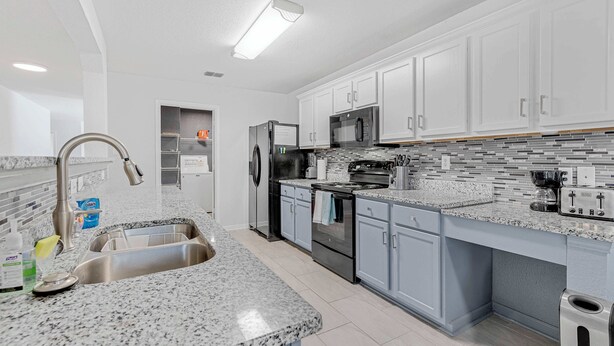 Una cocina moderna con armarios blancos, encimeras de granito, electrodomésticos de acero inoxidable y salpicadero de azulejos.