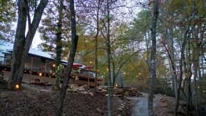 A forested area with a stone wall, a wooden deck, and string lights.