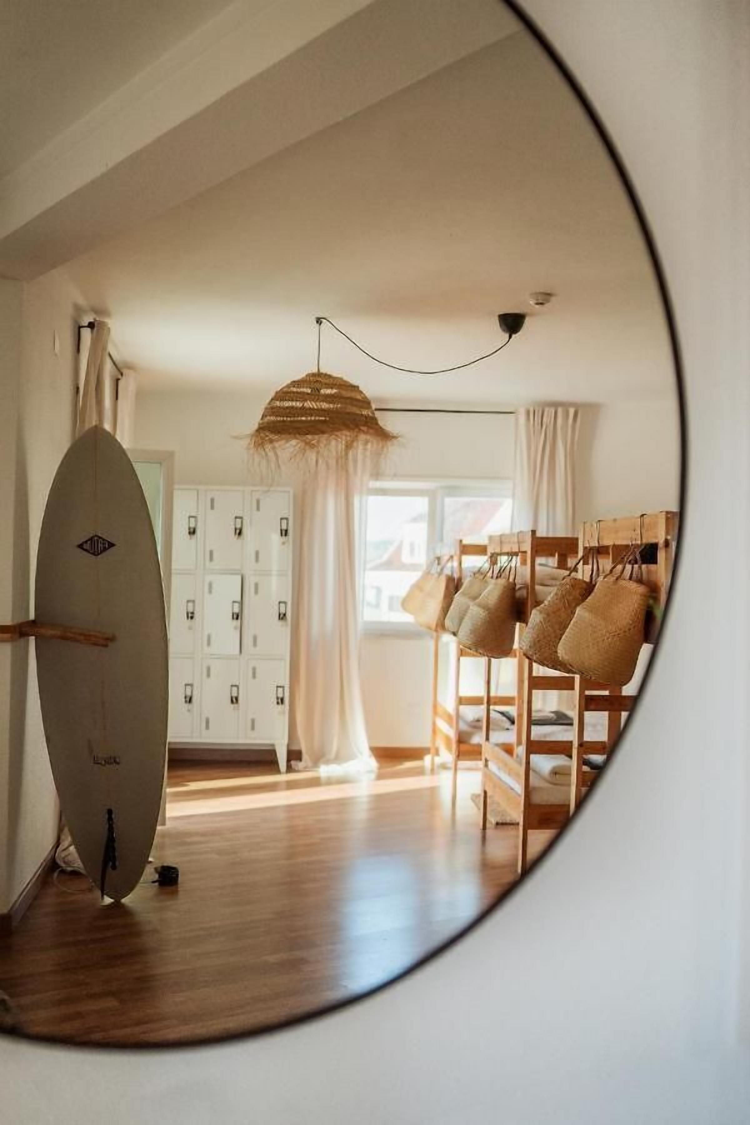 A room with a surfboard leaning against a wall, a wooden bench with cushions, and a hanging light fixture.